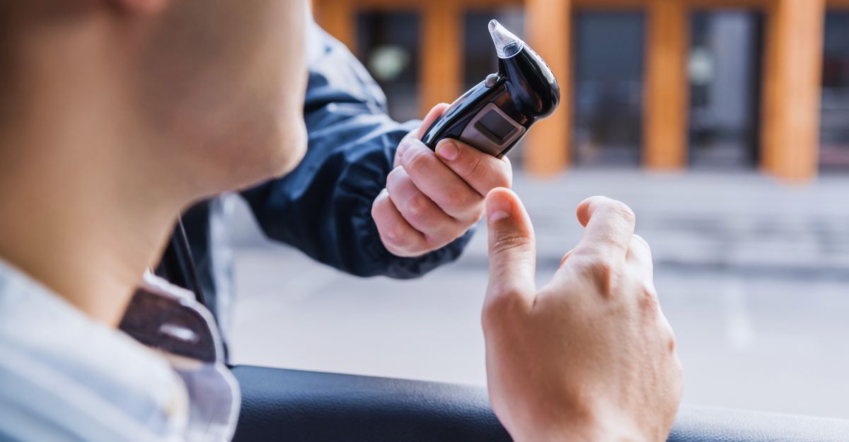 vista ritagliata di un poliziotto che somministra l'etilometro all'autista in auto, primo piano sfocato