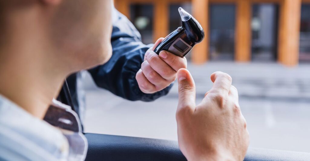 vista ritagliata di un poliziotto che somministra l'etilometro all'autista in auto, primo piano sfocato