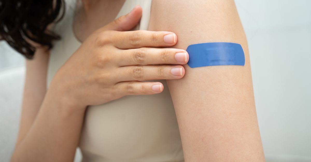 Primo piano di una persona che tocca un cerotto blu applicato sulla parte superiore del braccio dopo una vaccinazione