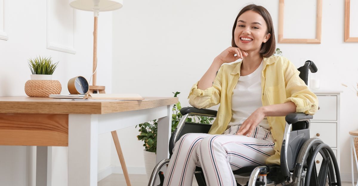 Una donna sorridente seduta su una sedia a rotelle in una stanza luminosa accanto a una scrivania