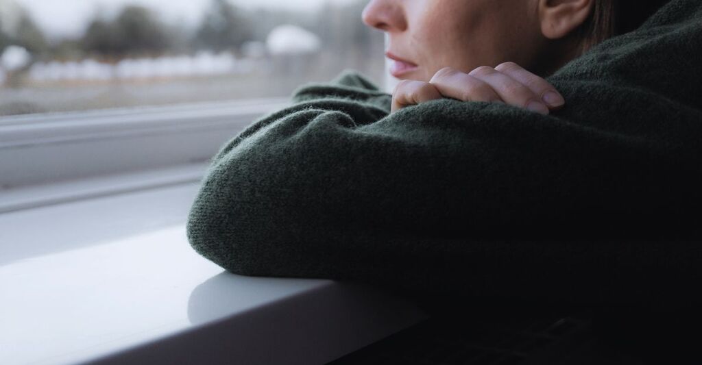 Donna triste e pensierosa seduta sul davanzale di una finestra. Salute mentale. Paesaggio invernale all'esterno.