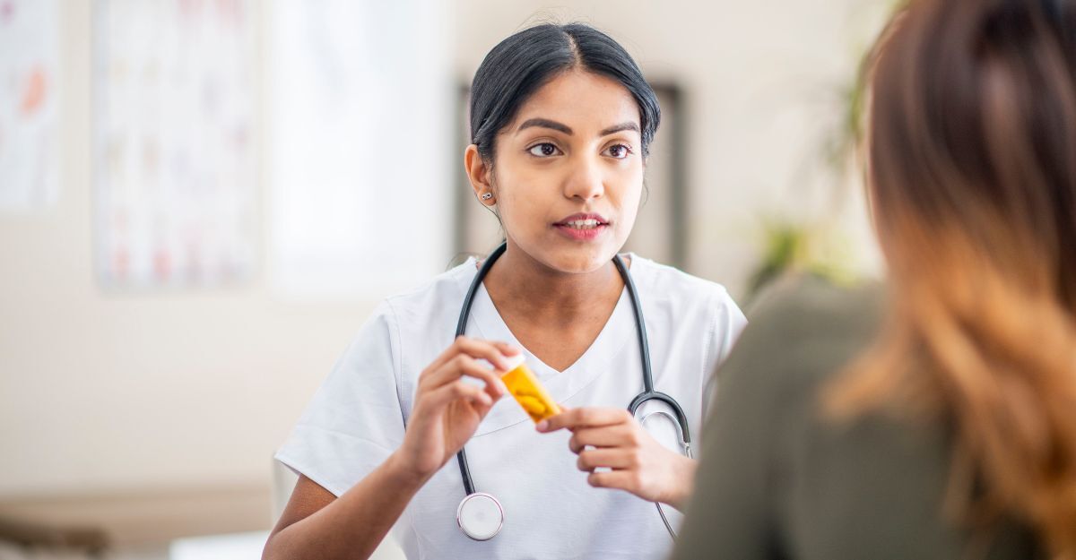 Una dottoressa in camice bianco spiega l'uso di un farmaco a una paziente tenendo in mano un flacone giallo