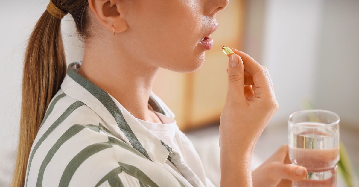 Donna con un bicchiere d'acqua che assume una pillola di vitamina a casa, primo piano