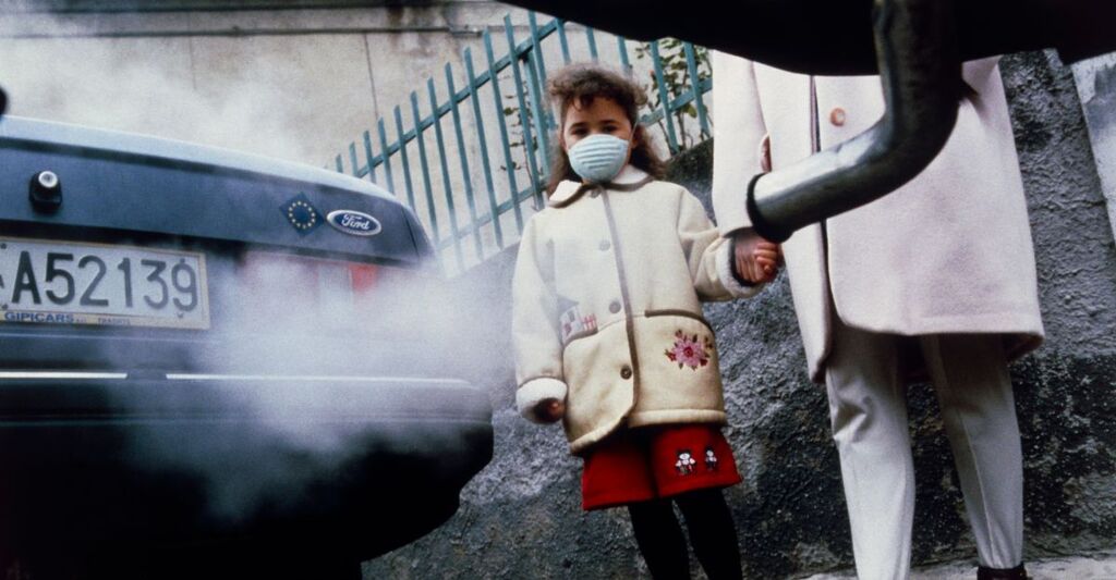 Una bambina ammalata di fianco in una città inquinata.