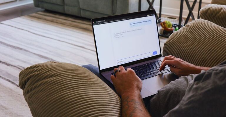 Uomo di mezza età in poltrona reclinabile color abbronzatura invia messaggi tramite chatbot con intelligenza artificiale