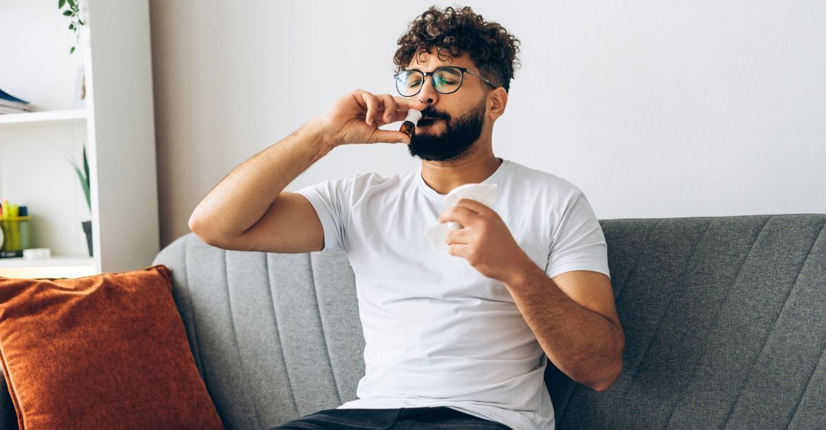 Un uomo mediorientale triste usa uno spray nasale per curare le allergie a casa, seduto sul divano