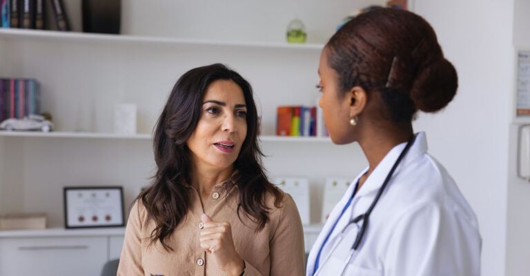 Una donna caucasica matura visita una giovane dottoressa africana per un consulto, raccontando informazioni sull'assistenza sanitaria e sui sintomi della malattia. Il medico compila un modulo medico e ascolta il paziente nell'ambulatorio.