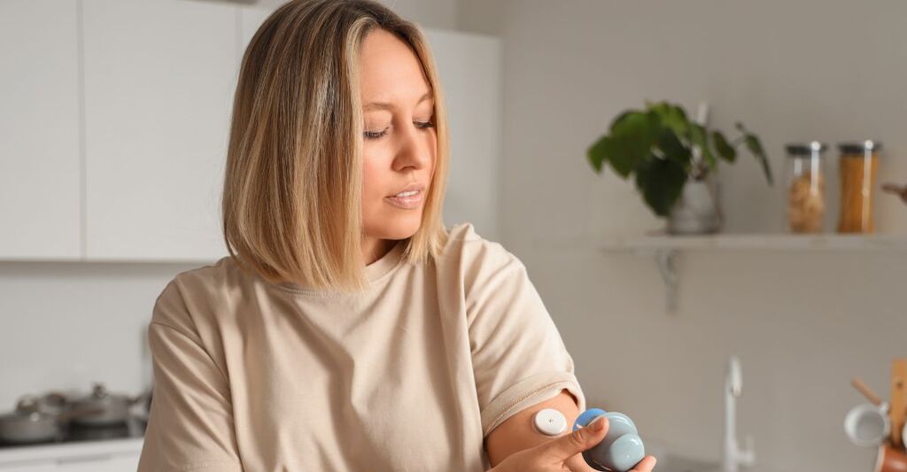 Una donna controlla un sensore per la glicemia applicato sulla parte superiore del braccio utilizzando un dispositivo di lettura portatile