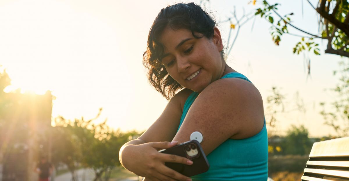Una donna all'aperto usa il suo smartphone per scansionare un sensore per il monitoraggio del glucosio applicato sul braccio