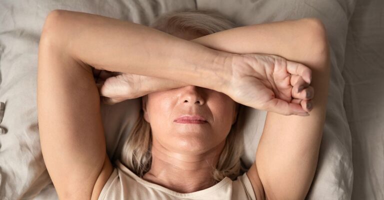 Donna con braccia incrociate sugli occhi che non riesce a dormire