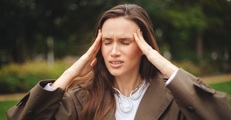 Ritratto di una donna dai lunghi capelli castani, frustrata, triste e sconvolta, su uno sfondo verde naturale, che soffre di mal di testa, emicrania e un forte dolore. La donna cammina in una giornata autunnale o primaverile. Stress o mal di testa.