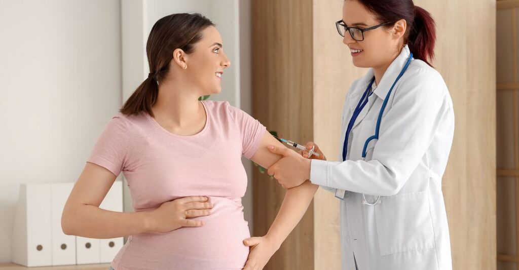 Una dottoressa in camice bianco somministra un vaccino a una donna incinta sorridente