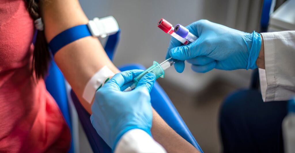 Un operatore sanitario con guanti azzurri esegue un prelievo di sangue dal braccio di un paziente