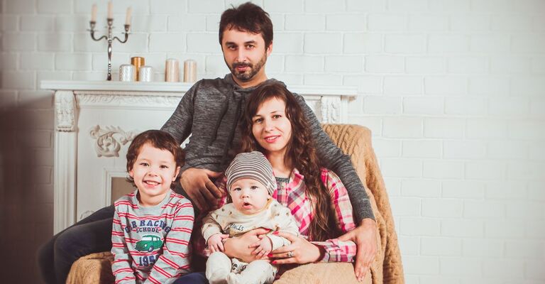 Ritratto fotografico di una famiglia composta da padre, madre e due bambini piccoli seduti insieme in casa