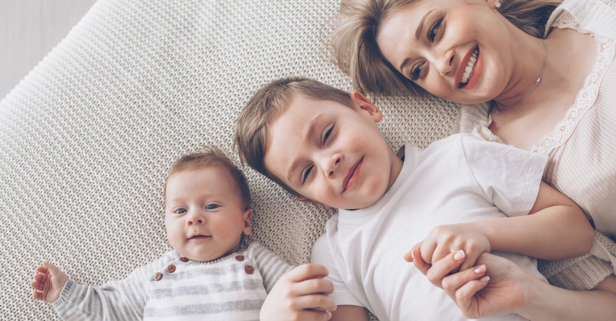 Una madre sorridente sdraiata su una superficie morbida insieme ai suoi due figli piccoli