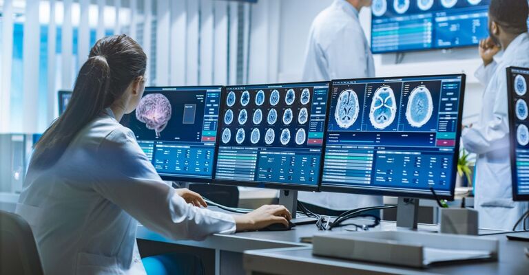Un team di scienziati professionisti lavora nel laboratorio di ricerca sul cervello. Neurologi e neuroscienziati, circondati da monitor che mostrano scansioni TC e RM, discutono e lavorano al computer.