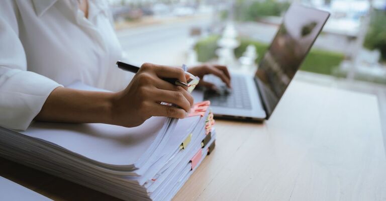 Una donna con una camicia rossa sta maneggiando un gran numero di documenti e fascicoli. Lavoro d'ufficio, la documentazione, l'organizzazione, la gestione, le scadenze, i carichi di lavoro, la burocrazia e le responsabilità aziendali.