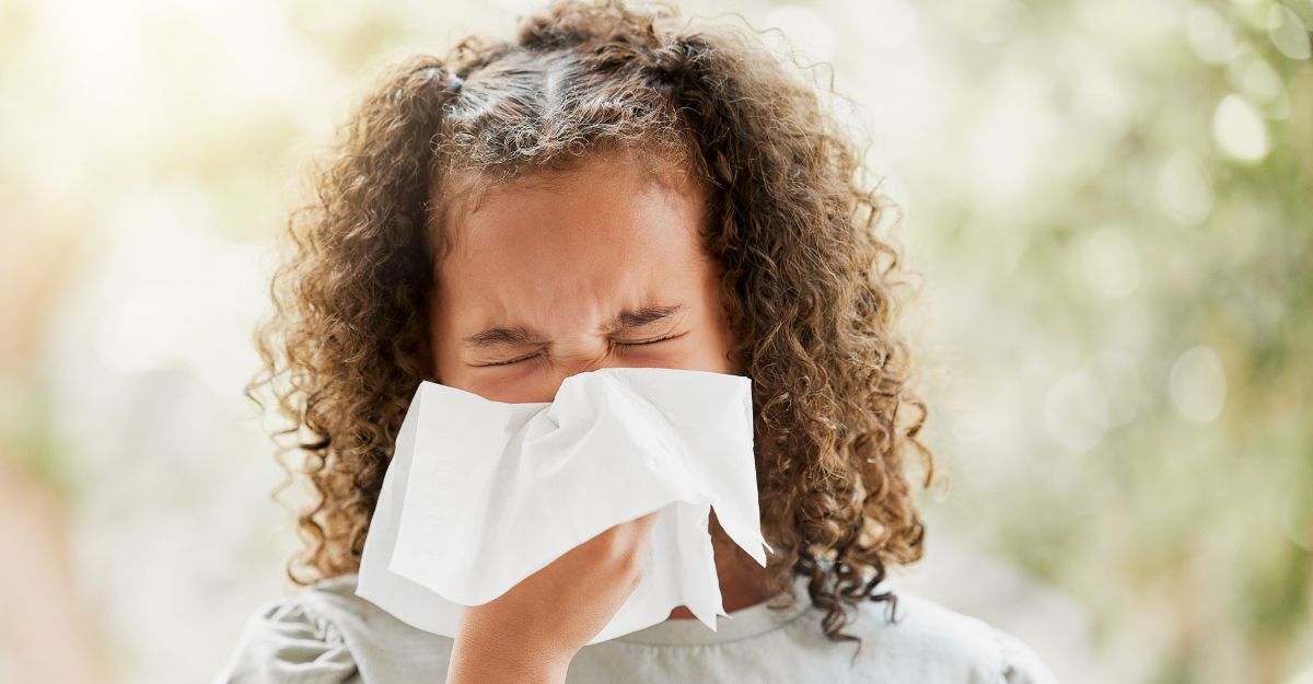 Bambina malata con l'influenza, si soffia il naso e sembra a disagio. Bambina che soffre di sinusite, allergie o sintomi di Covid e non si sente bene. Bambina con il raffreddore che starnutisce e tiene in mano un fazzoletto.