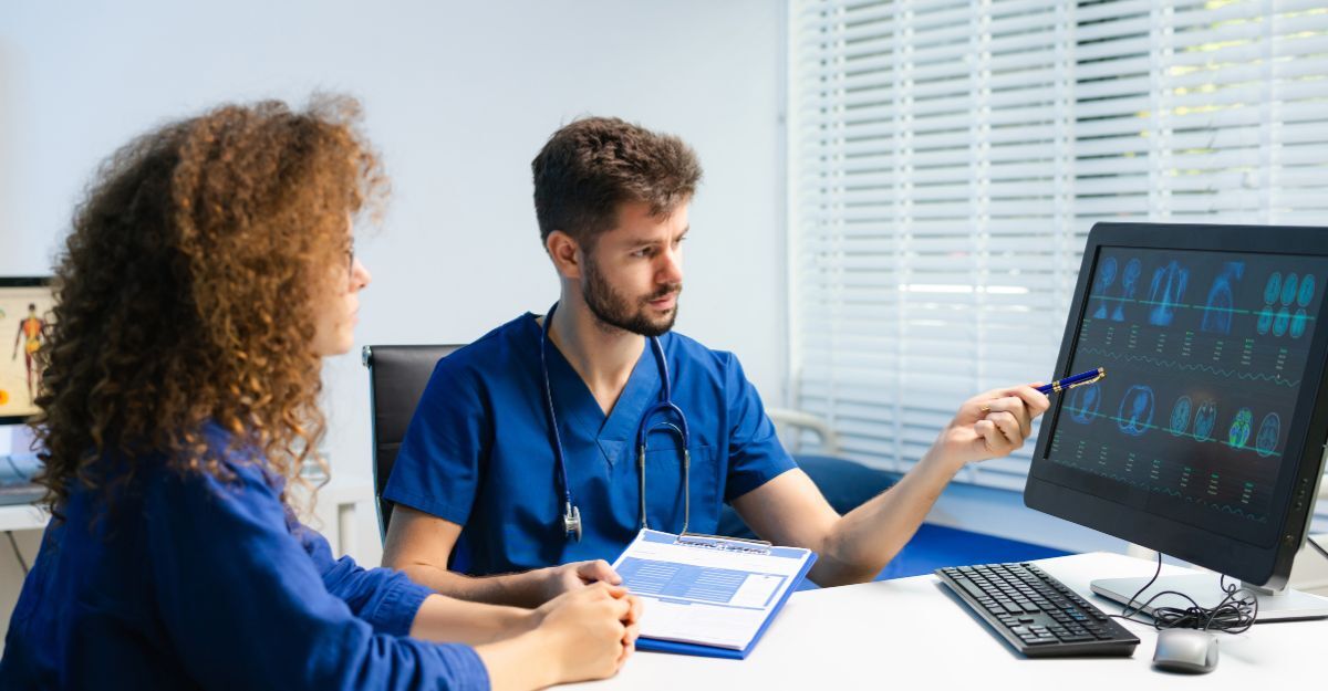 Un medico in camice blu mostra dei risultati clinici su un monitor a una paziente seduta di fronte a lui.