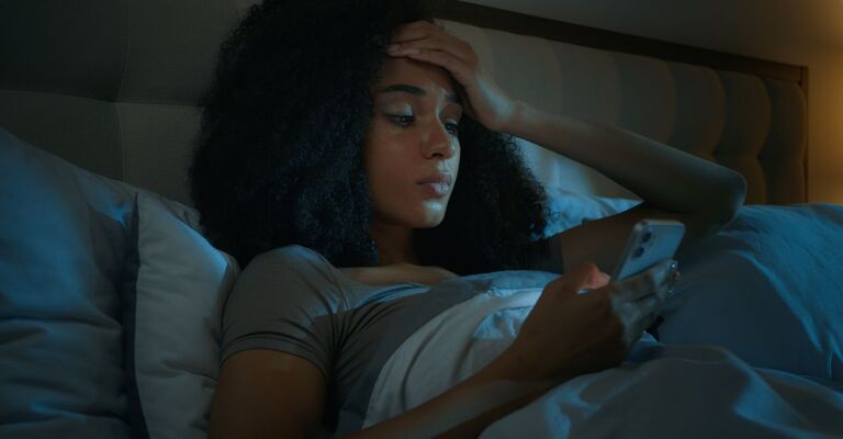 Ragazza afroamericana che scorre lo smartphone, app online sul telefono a letto prima di dormire, sconvolta, scioccata, donna di etnia cliente preoccupata, problema di internet, perdita di connessione, errore, cattiva notizia, rifiuto