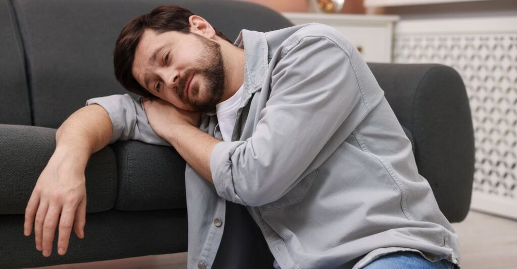 Un uomo con la barba che riposa la testa sul braccio, stanco, appoggiato a un divano.