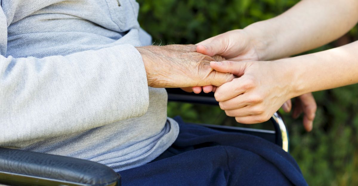Primo piano di una persona giovane che stringe con cura le mani di un anziano seduto in sedia a rotelle