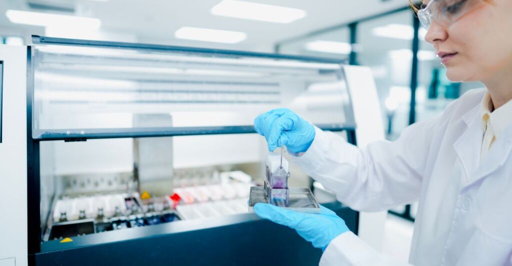 Tecnico di patologia che tiene in mano il porta-vetrini per biopsia per il controllo di qualità in laboratorio clinico. Scienziato medico che prepara sezioni di tessuto per la diagnosi oncologica microscopica.