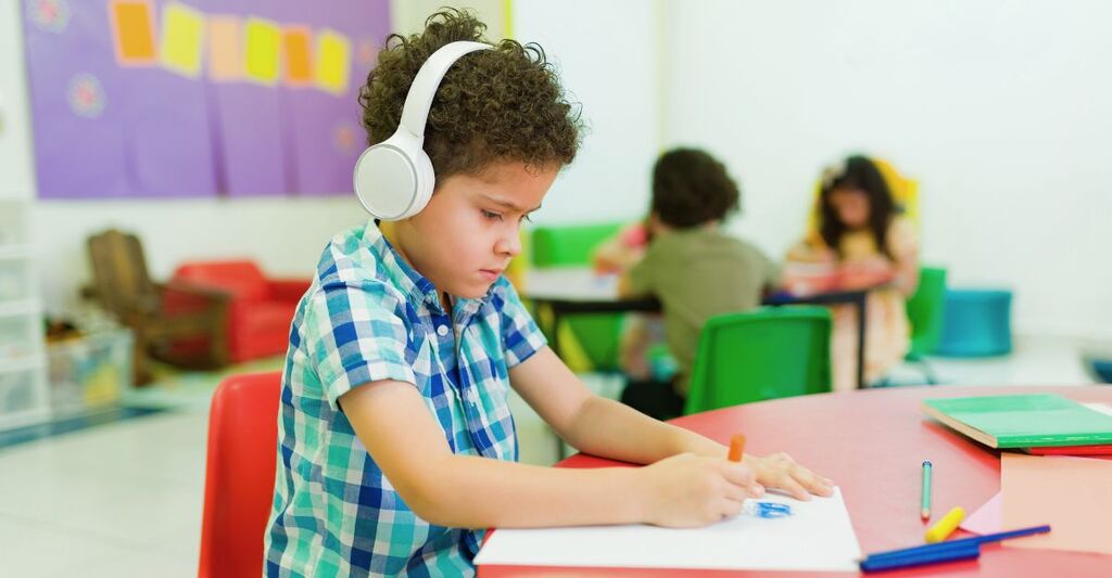 Un bambino autistico in età prescolare con le cuffie colora da solo in classe