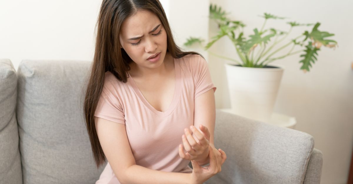 Una giovane donna seduta su un divano che si massaggia il polso con un'espressione dolorante