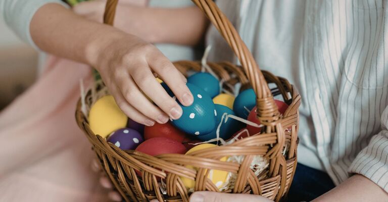 Primo piano di mani che tengono un cestino di vimini pieno di uova di Pasqua colorate e decorate