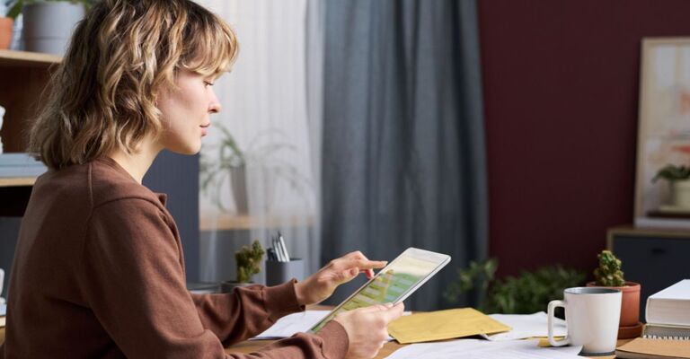 Una donna di profilo seduta a una scrivania mentre utilizza un tablet