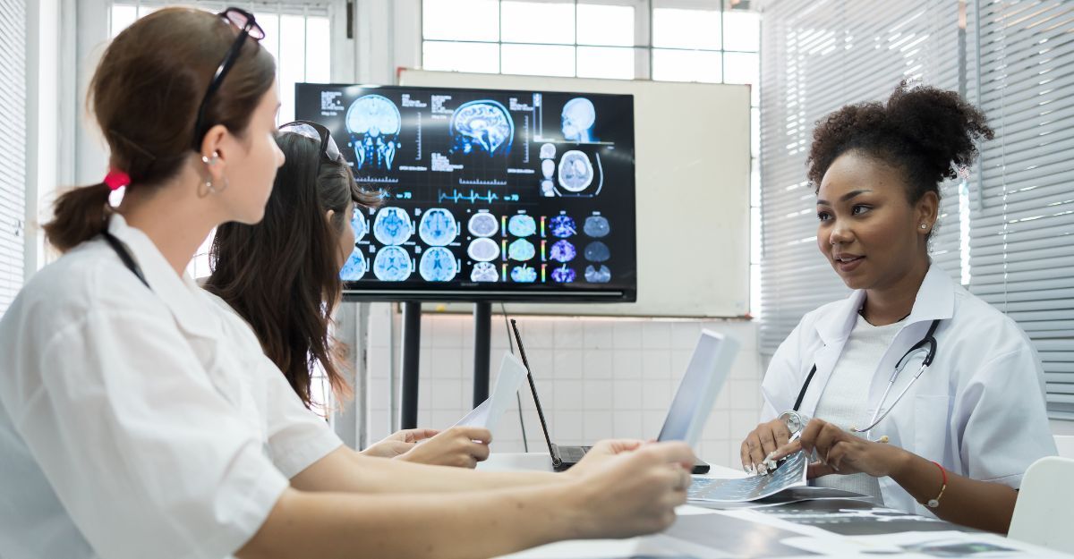 Un'équipe di medici si riunisce nel laboratorio di ricerca sul cervello, con un monitor che mostra immagini di risonanza magnetica e TAC cerebrali. Un gruppo di dottoresse discute di interventi chirurgici e trattamenti, con l'ausilio di radiografie.