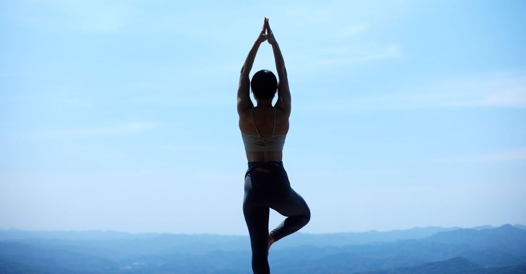 Una persona di spalle in una posizione di yoga all'aperto con vista sulle montagne.