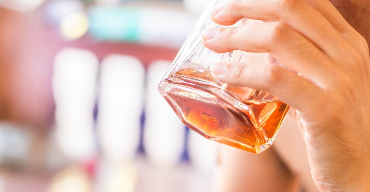 Primo piano di una persona che beve un bicchiere di liquore ambrato.