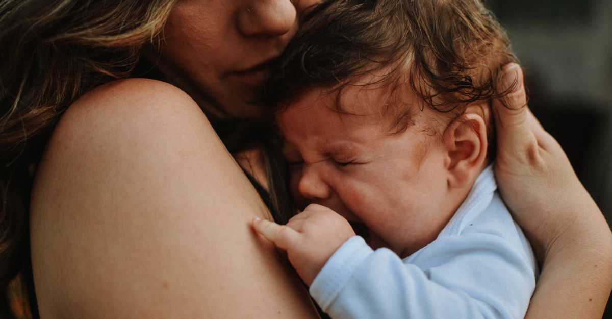 Primo piano di un neonato che piange tra le braccia di un genitore per essere confortato.