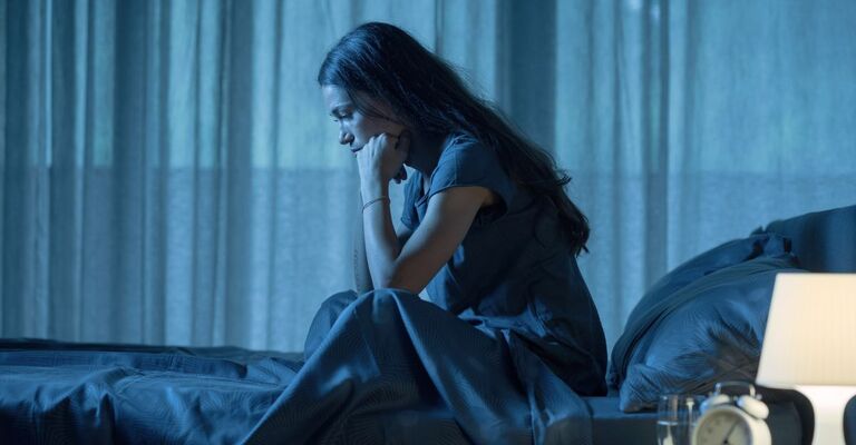 giovane donna sveglia e seduta sul letto a causa dell'insonnia