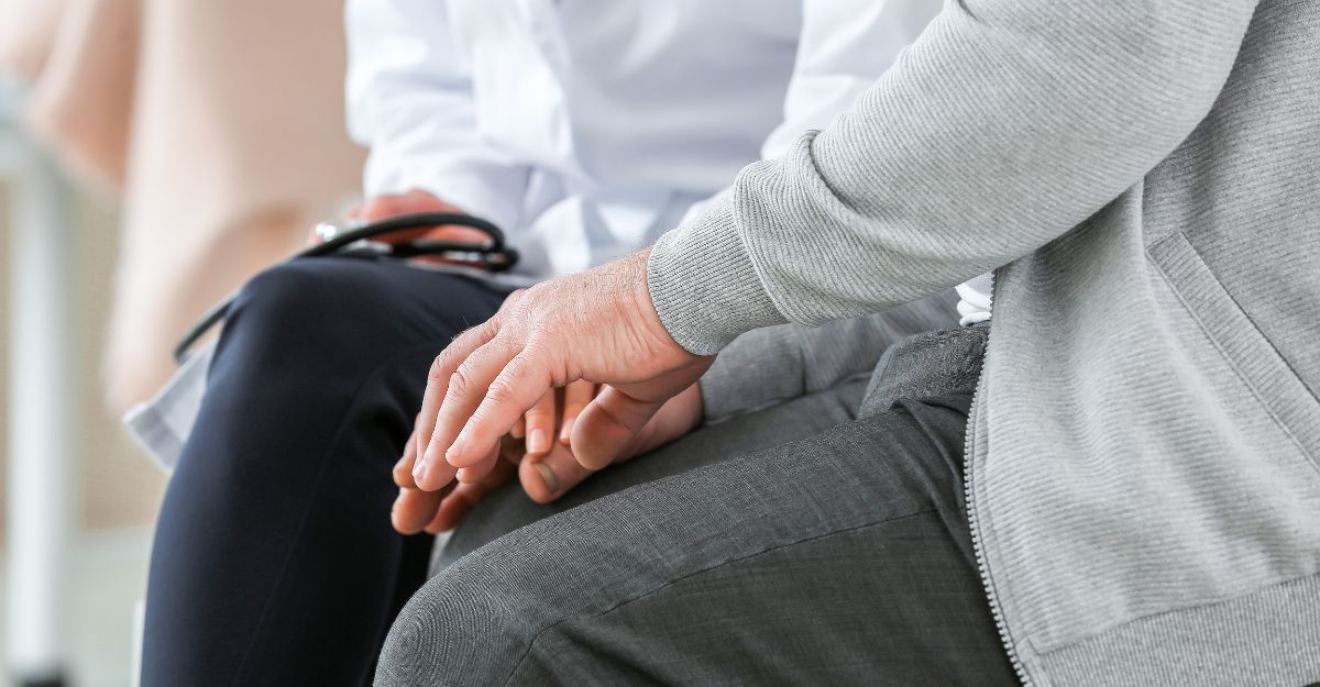 Primo piano di un medico che poggia una mano sulla mano di un paziente seduto, in segno di supporto e conforto.