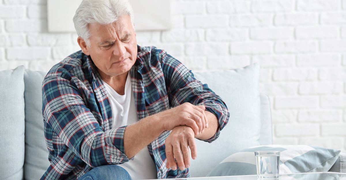 Un uomo anziano seduto sul divano che si tiene il polso con un'espressione sofferente