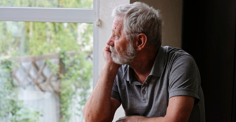 Un anziano pensionato è seduto da solo in casa che guarda fuori dalla finestra.