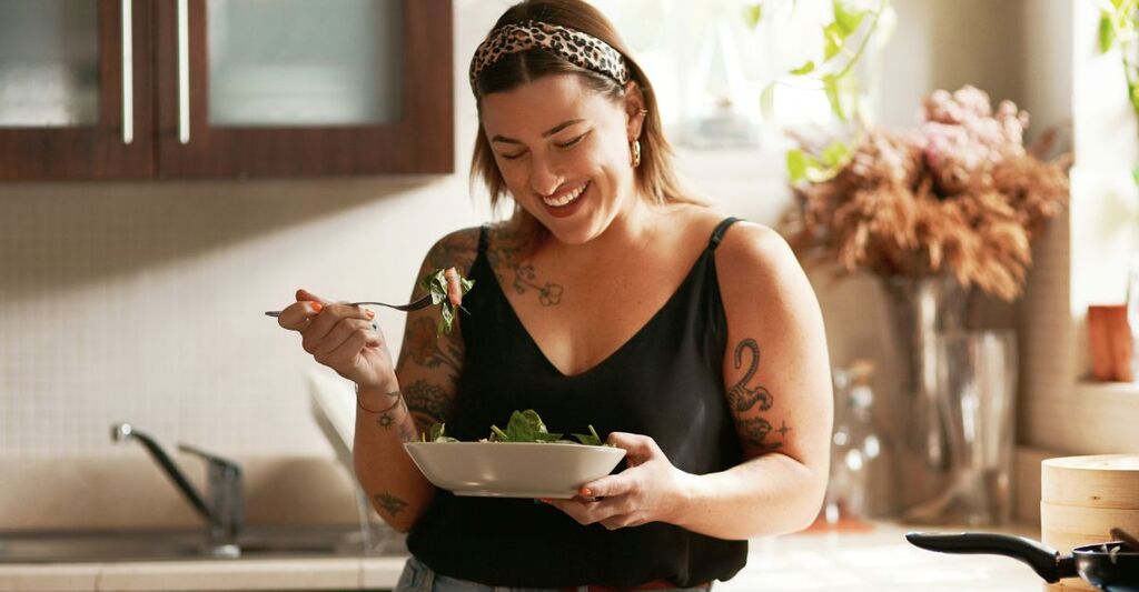 Donna, dieta e persona che mangia insalata nella sua cucina di casa ed è felice per un pasto nutriente o un pranzo sano. Sorriso, cibo e giovane donna vegana nel suo appartamento o casa e mangia verdure