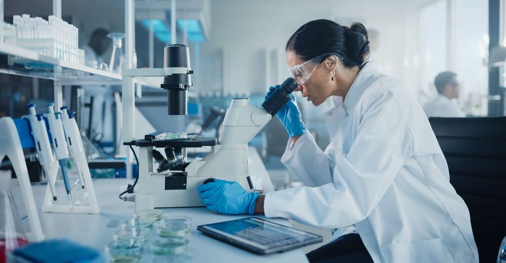 Laboratorio di sviluppo medico: una scienziata caucasica osserva al microscopio un campione in una piastra di Petri. Specialisti impegnati nella ricerca medica e biotecnologica in un laboratorio farmaceutico all'avanguardia.