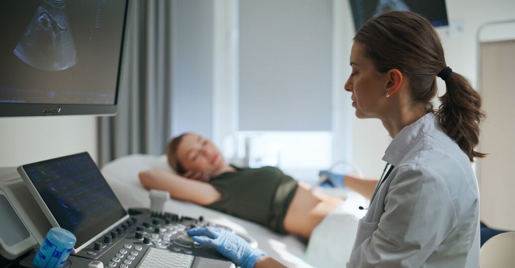 Medico specialista che esamina una paziente incinta con un'apparecchiatura ecografica (primo piano) in clinica