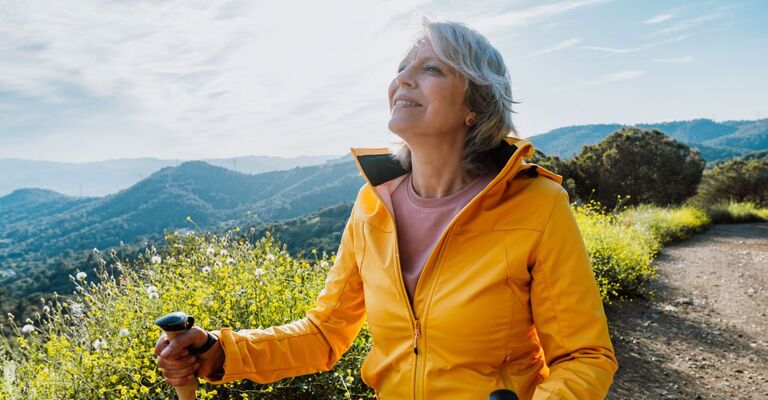 Anziana attiva che fa escursione su un sentiero all'aperto con l'ausilio di bastoncini da trekking