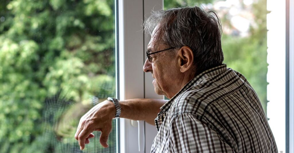 Persona anziana che guarda fuori da una finestra indossando un paio di occhiali