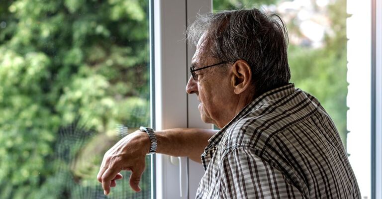 Persona anziana che guarda fuori da una finestra indossando un paio di occhiali