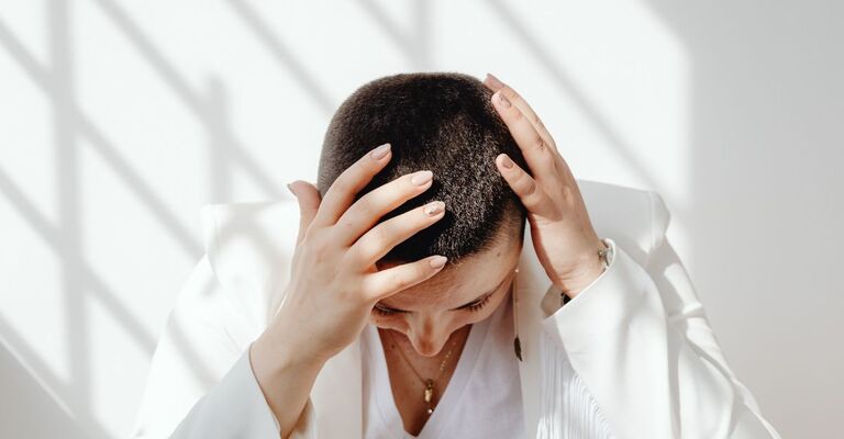 Una donna con tricodinia si tocca la testa per il dolore ai capelli.