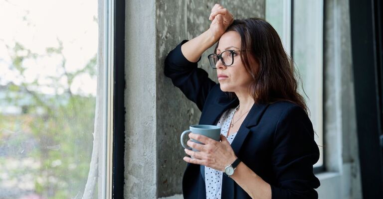 donna sui 45 anni, guarda dalla finestra con in mano una tazza 