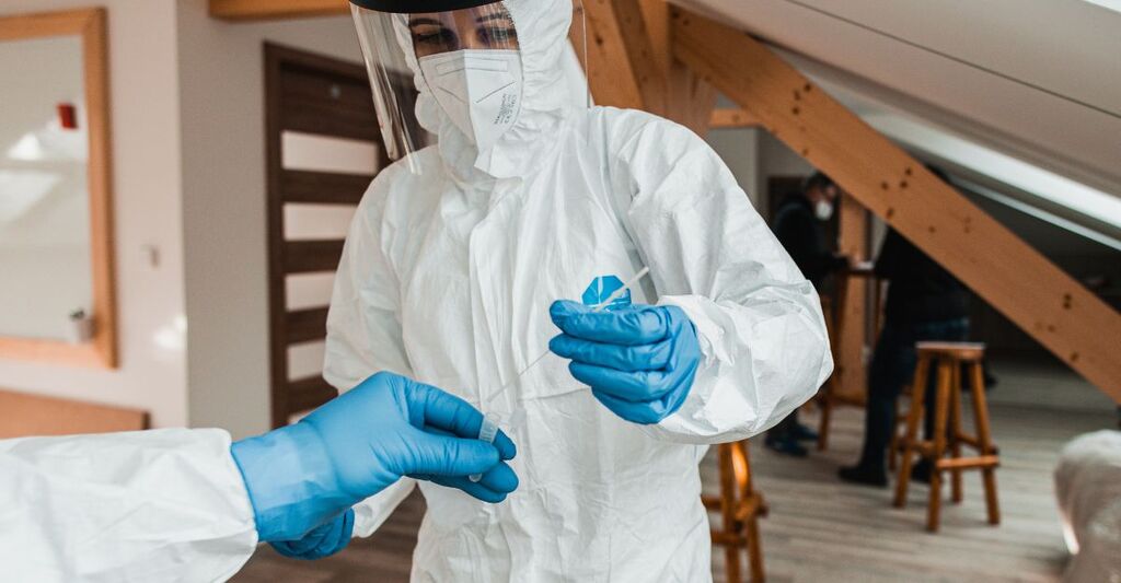 Operatore sanitario in tuta protettiva completa e visiera che maneggia un tampone medico