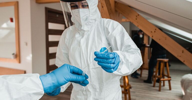 Operatore sanitario in tuta protettiva completa e visiera che maneggia un tampone medico