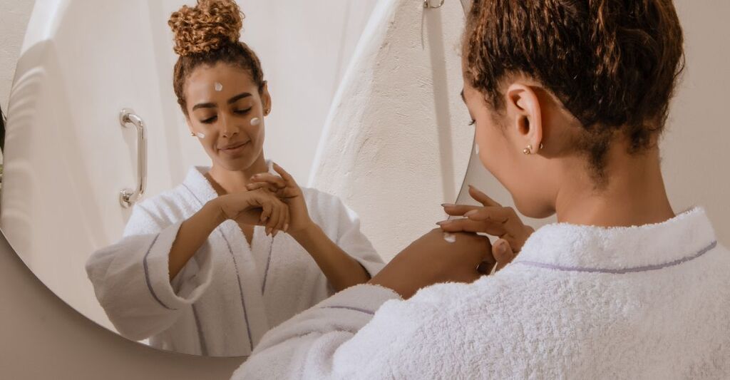 ragazza si applica la crema sul viso, davanti allo specchio